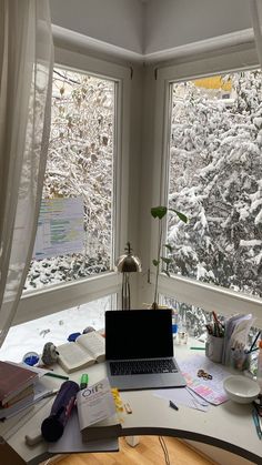 a laptop computer sitting on top of a desk in front of two windows covered in snow