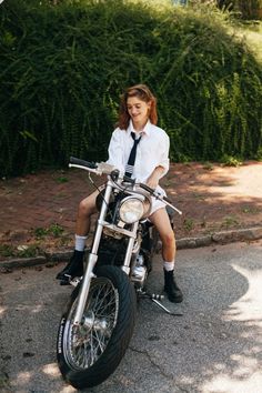 a woman sitting on the back of a motorcycle wearing a tie and dress shirt with short shorts