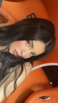 a woman with long black hair laying on an orange couch