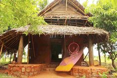 a small hut with a thatched roof and some decorations on the front porch, surrounded by trees