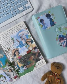 a teddy bear and book on a bed next to a computer keyboard with an open notebook