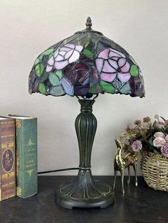 a lamp that is on top of a table next to some books and flowers in a basket