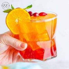 a hand holding a glass filled with orange juice and cranberries on the rim