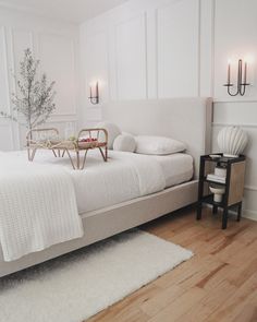 a white bed sitting in a bedroom next to a table with two candles on it