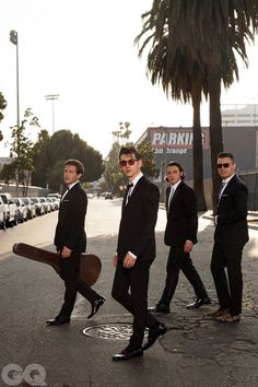 three men in suits and sunglasses walking down the street with a large piece of wood