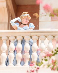 a woman in a blue dress is looking over a balcony railing with her hand on her head