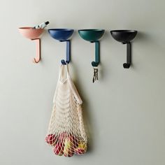 three bowls and two spoons hanging from hooks on the wall, one with a net bag