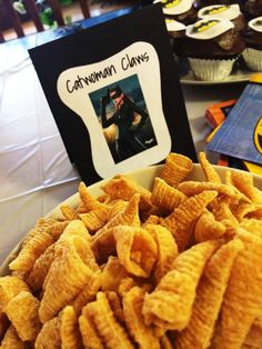 a bowl filled with corn flakes next to cupcakes and a sign on the table