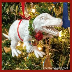 a white dinosaur ornament hanging from a christmas tree with red and green ornaments