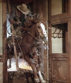 a man riding on the back of a brown horse through a wooden doorway next to a white horse