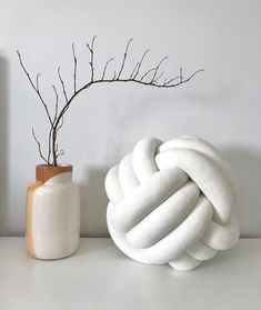 a white vase with a branch in it next to a knot sculpture on a table