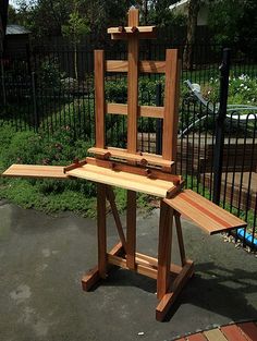 a wooden easel sitting on top of a cement ground next to a fenced in area