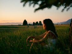 a woman sitting in the middle of a field at sunset