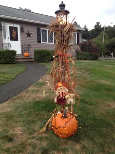 a scarecrow sitting on top of a pumpkin in front of a house with lights