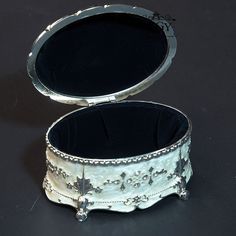 an ornate silver jewelry box sitting on a black surface with its lid open and the lid closed