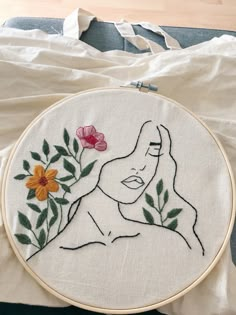 a woman's face with flowers in her hand is embroidered onto a white piece of fabric