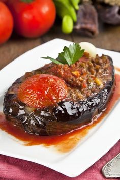 an eggplant stuffed with meat and tomato sauce on a plate next to some vegetables