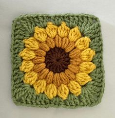 a crocheted square with a yellow and green flower on it's center