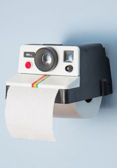 a polaroid camera mounted to a wall next to a roll of toilet paper