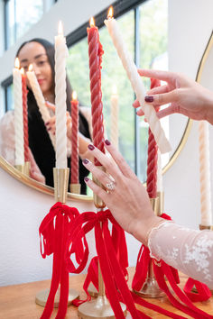 a woman is lighting candles on a table with red ribbon around her hands and another woman in the background