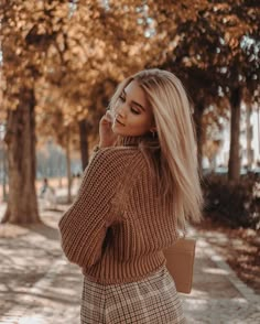 a woman with long blonde hair wearing a brown sweater and plaid skirt