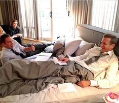 two men in suits and ties are laying on a bed with one man pointing at the camera