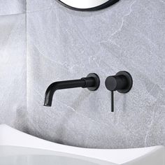 a black faucet on the wall next to a white sink and round mirror