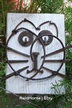 a close up of a metal cat face on a sign with trees in the background