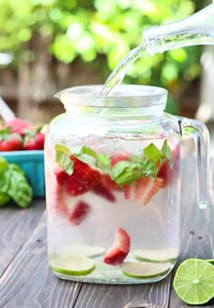 a pitcher filled with water and strawberries on top of a table next to sliced limes