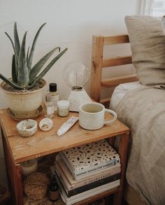 a wooden table topped with books next to a plant on top of a bed covered in blankets