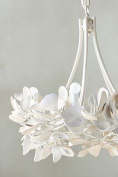 a chandelier with white flowers hanging from it's sides and leaves on the bottom