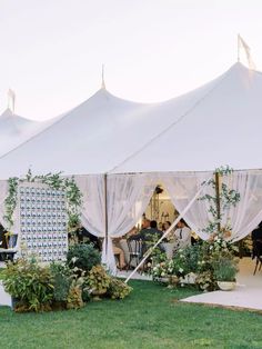 an outdoor tent with white curtains and greenery on the lawn, set up for a wedding reception