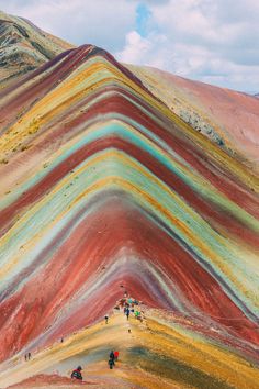 people are walking on the side of a mountain with colorful hills in the back ground