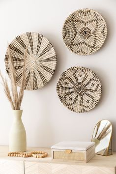 three woven plates are hanging on the wall next to a vase with dried grass in it