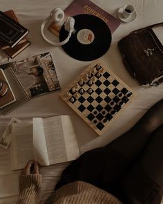 a person laying in bed reading a book next to a chess board and other items