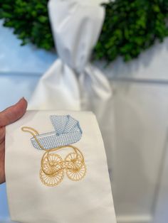 a hand holding a napkin with a baby carriage embroidered on it