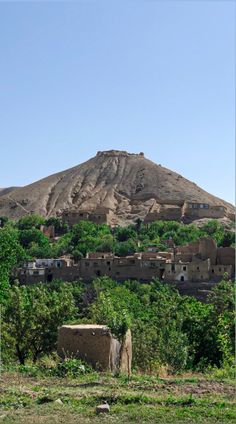 an old village sits in the middle of a green valley with a mountain in the background