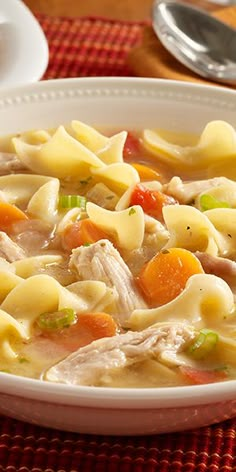 a white bowl filled with chicken noodle soup on top of a red place mat