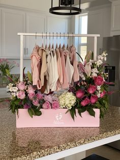 a pink box with flowers and clothes hanging from it's hooks on a kitchen counter