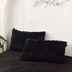 two black pillows sitting on top of a bed next to a plant in a white room