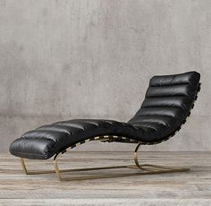 a black leather chaise lounge chair sitting on top of a wooden floor next to a concrete wall