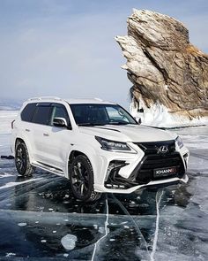 a white suv is parked on ice near a large rock