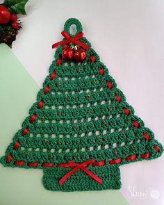 a crocheted christmas tree ornament hanging on a green surface with red ribbon