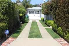 a driveway leading to a house with trees and bushes on both sides, in front of a white garage