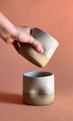 a person is throwing something into a small ceramic cup on a pink surface with a hand reaching for it