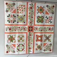 an orange and green quilt hanging on a wall next to a white shelf with a pair of scissors in it