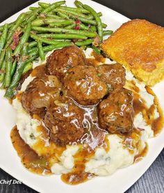 a white plate topped with meatballs, mashed potatoes and gravy next to green beans