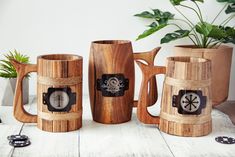 three wooden mugs sitting next to each other on top of a white table with plants in the background