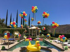 an inflatable rubber duck floating on top of a pool surrounded by balloons