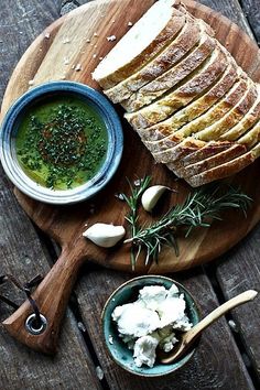 bread, butter and herbs on a cutting board next to a bowl of green soup